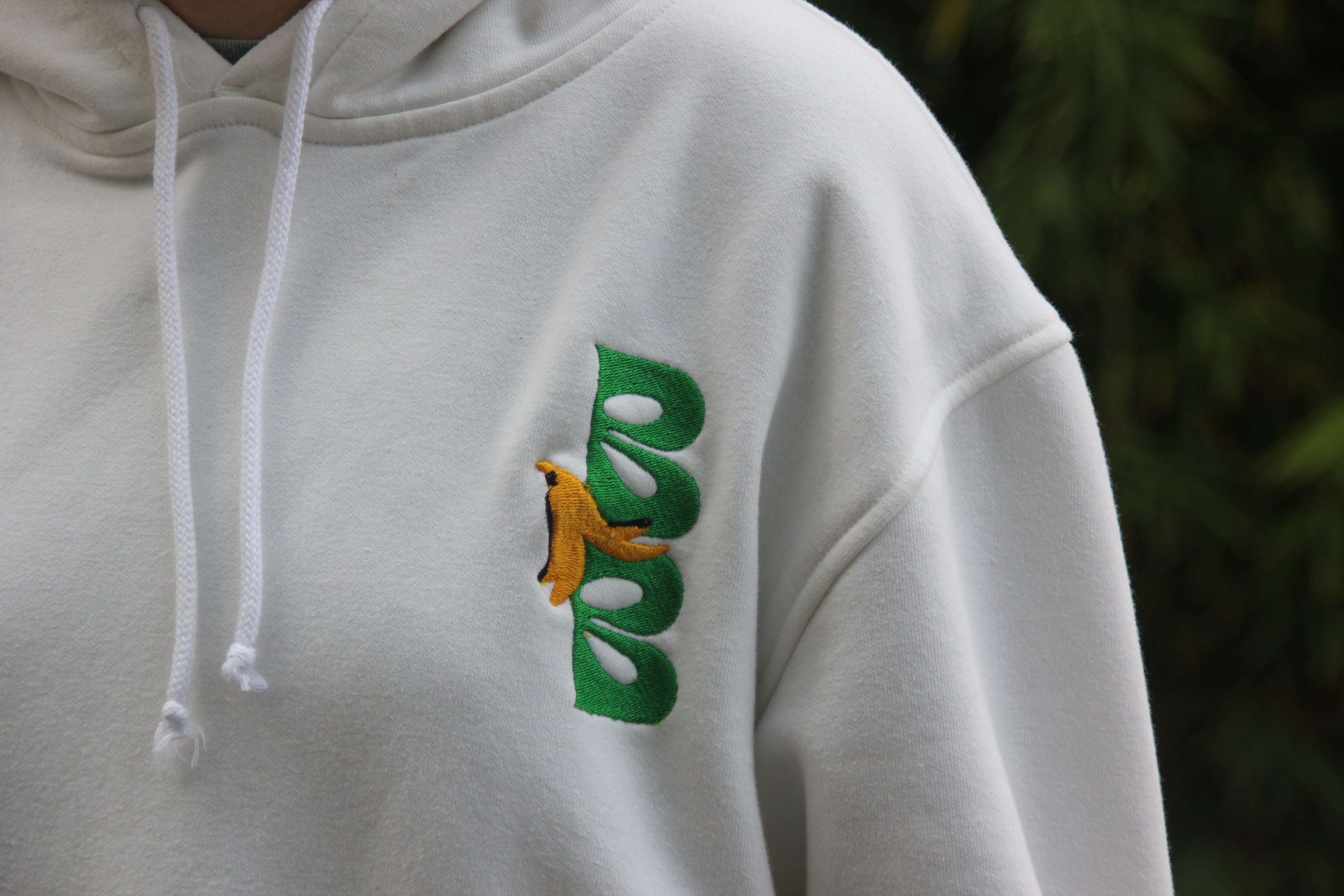 hoodie blanco Baked Banana con logo bordado verde y diseño de banana